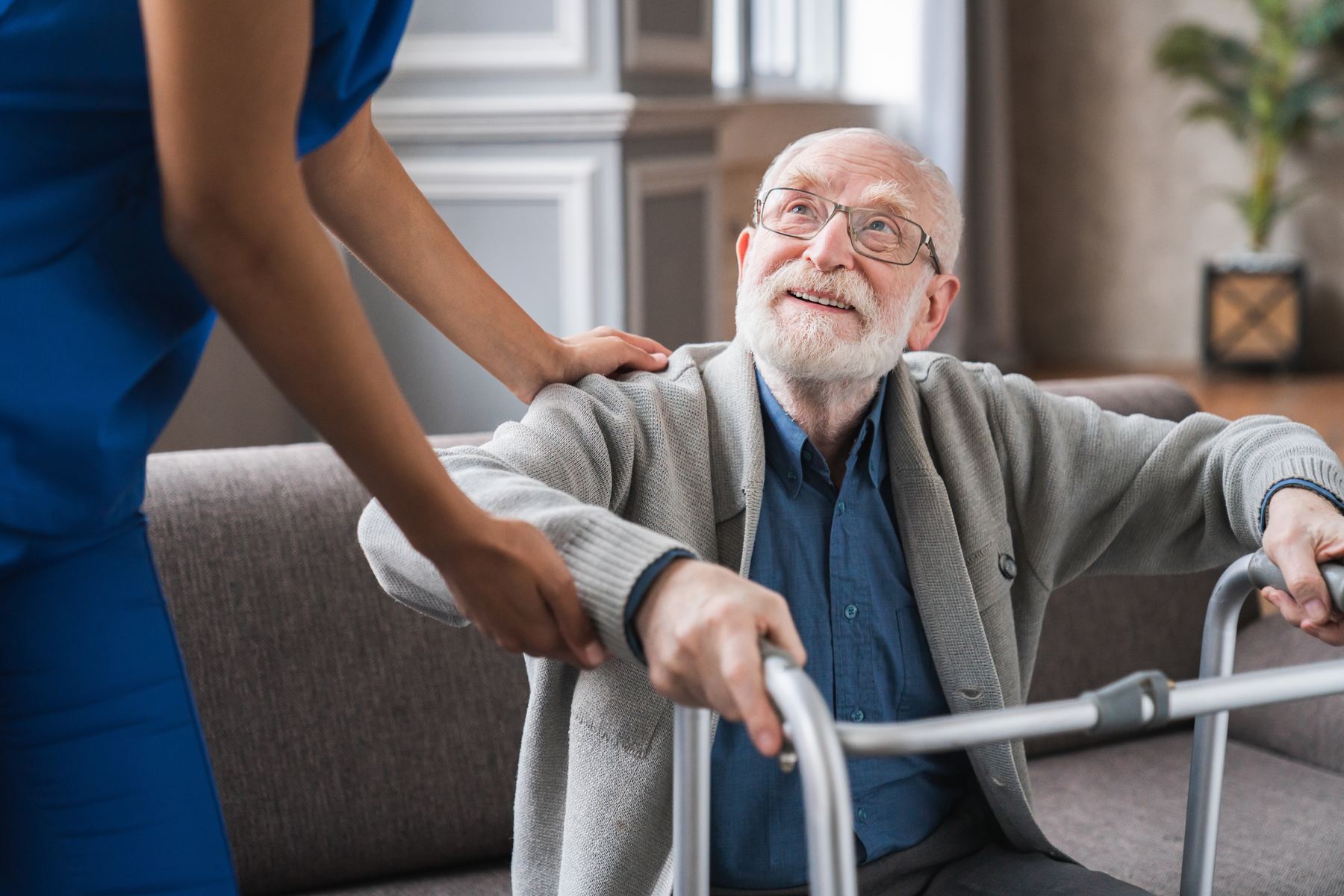 A carer's hand supporting an elderly man using a walking frame